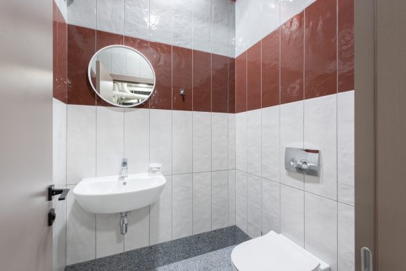 Small business restroom with red and white tile, small round mirror and white sink and toilet.